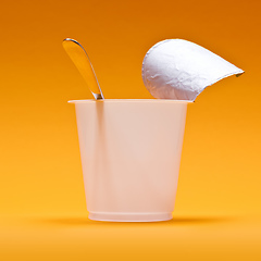 Image showing empty clean yogurt cup with spoon on an orange background