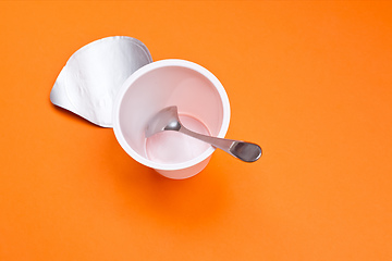 Image showing empty clean yogurt cup with spoon on an orange background