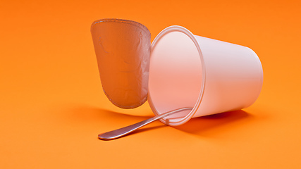 Image showing empty clean yogurt cup with spoon on an orange background