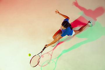 Image showing Young woman in blue shirt playing tennis in mixed light. Youth, flexibility, power and energy.