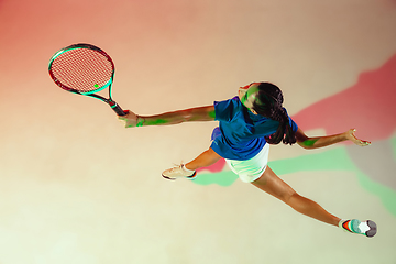 Image showing Young woman in blue shirt playing tennis in mixed light. Youth, flexibility, power and energy.