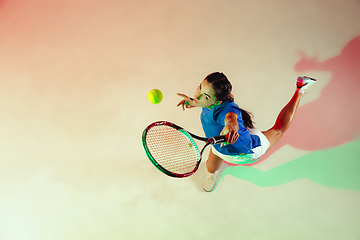 Image showing Young woman in blue shirt playing tennis in mixed light. Youth, flexibility, power and energy.