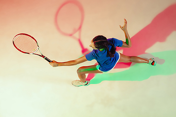 Image showing Young woman in blue shirt playing tennis in mixed light. Youth, flexibility, power and energy.