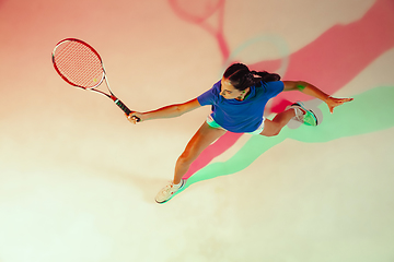 Image showing Young woman in blue shirt playing tennis in mixed light. Youth, flexibility, power and energy.