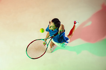 Image showing Young woman in blue shirt playing tennis in mixed light. Youth, flexibility, power and energy.