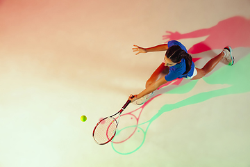 Image showing Young woman in blue shirt playing tennis in mixed light. Youth, flexibility, power and energy.