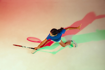 Image showing Young woman in blue shirt playing tennis in mixed light. Youth, flexibility, power and energy.