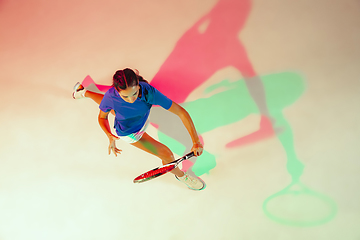 Image showing Young woman in blue shirt playing tennis in mixed light. Youth, flexibility, power and energy.