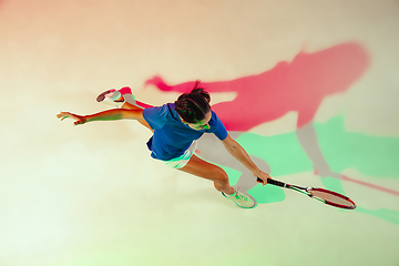 Image showing Young woman in blue shirt playing tennis in mixed light. Youth, flexibility, power and energy.