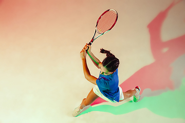 Image showing Young woman in blue shirt playing tennis in mixed light. Youth, flexibility, power and energy.