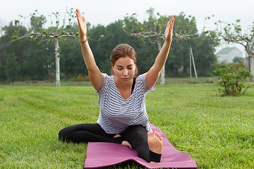 Image showing Young beautiful woman doing yoga exercise in green park. Healthy lifestyle and fitness concept.