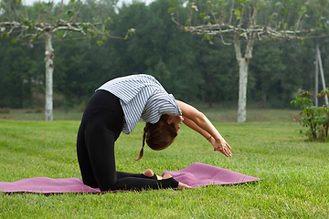 Image showing Young beautiful woman doing yoga exercise in green park. Healthy lifestyle and fitness concept.