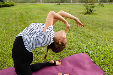 Image showing Young beautiful woman doing yoga exercise in green park. Healthy lifestyle and fitness concept.