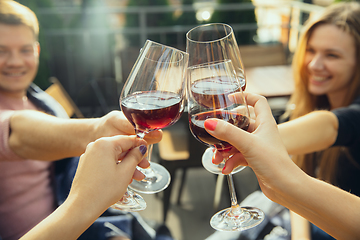 Image showing People clinking glasses with wine on the summer terrace of cafe or restaurant. Close up shot, lifestyle.