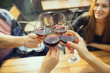 Image showing People clinking glasses with wine on the summer terrace of cafe or restaurant. Close up shot, lifestyle.