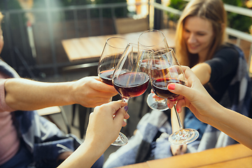 Image showing People clinking glasses with wine on the summer terrace of cafe or restaurant. Close up shot, lifestyle.