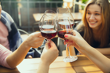 Image showing People clinking glasses with wine on the summer terrace of cafe or restaurant. Close up shot, lifestyle.