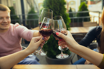 Image showing People clinking glasses with wine on the summer terrace of cafe or restaurant. Close up shot, lifestyle.