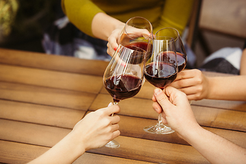 Image showing People clinking glasses with wine on the summer terrace of cafe or restaurant. Close up shot, lifestyle.