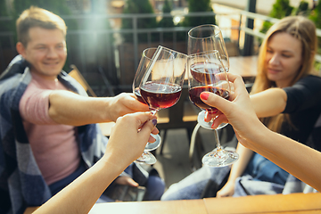 Image showing People clinking glasses with wine on the summer terrace of cafe or restaurant. Close up shot, lifestyle.