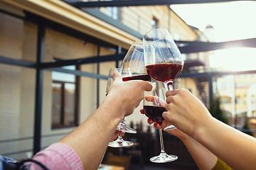 Image showing People clinking glasses with wine on the summer terrace of cafe or restaurant. Close up shot, lifestyle.