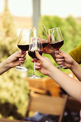 Image showing People clinking glasses with wine on the summer terrace of cafe or restaurant. Close up shot, lifestyle.