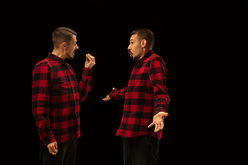 Image showing Young handsome man arguing with himself on black studio background.