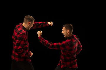 Image showing Young handsome man arguing with himself on black studio background.