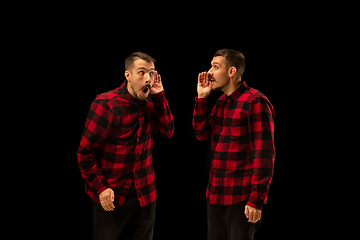 Image showing Young handsome man arguing with himself on black studio background.