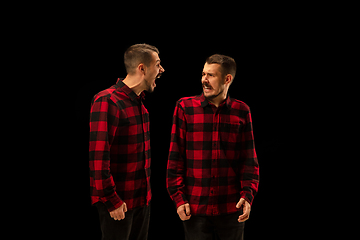 Image showing Young handsome man arguing with himself on black studio background.