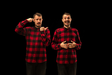 Image showing Young handsome man arguing with himself on black studio background.