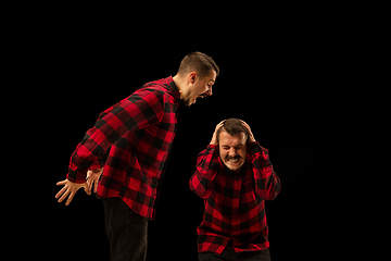 Image showing Young handsome man arguing with himself on black studio background.