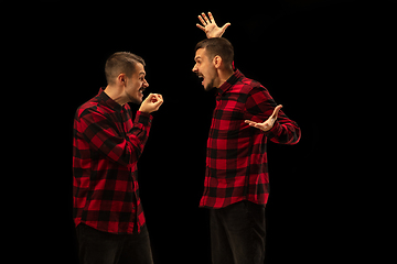 Image showing Young handsome man arguing with himself on black studio background.