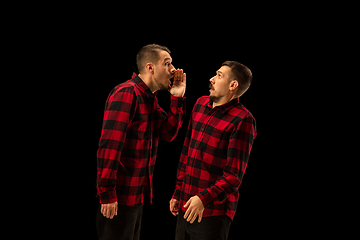 Image showing Young handsome man arguing with himself on black studio background.