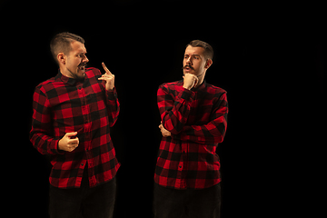 Image showing Young handsome man arguing with himself on black studio background.