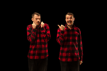 Image showing Young handsome man arguing with himself on black studio background.