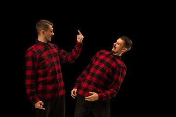 Image showing Young handsome man arguing with himself on black studio background.