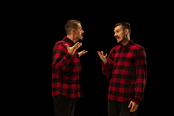 Image showing Young handsome man arguing with himself on black studio background.