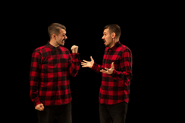 Image showing Young handsome man arguing with himself on black studio background.