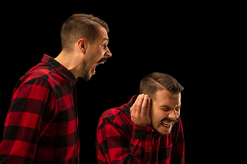 Image showing Young handsome man arguing with himself on black studio background.