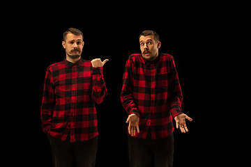 Image showing Young handsome man arguing with himself on black studio background.