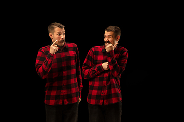 Image showing Young handsome man arguing with himself on black studio background.