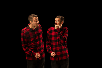 Image showing Young handsome man arguing with himself on black studio background.