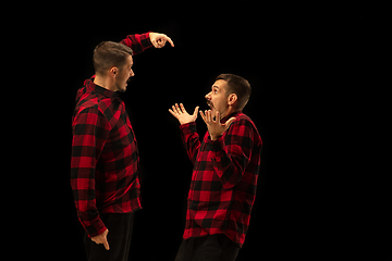 Image showing Young handsome man arguing with himself on black studio background.