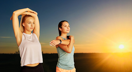 Image showing women with fitness trackers stretching outdoors