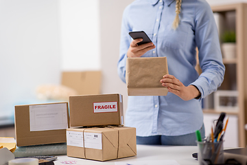 Image showing woman with smartphone and parcels at post office