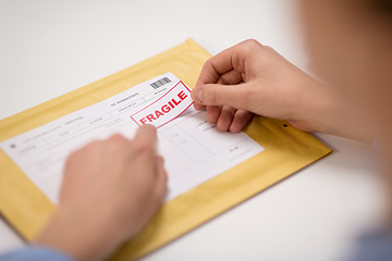 Image showing hands sticking fragile marks to parcel in envelope