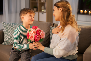 Image showing smiling little son gives flowers to mother at home