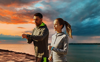 Image showing couple with fitness trackers running over sea