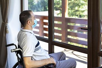 Image showing young man wearing face mask sitting in a wheelchair alone lookin